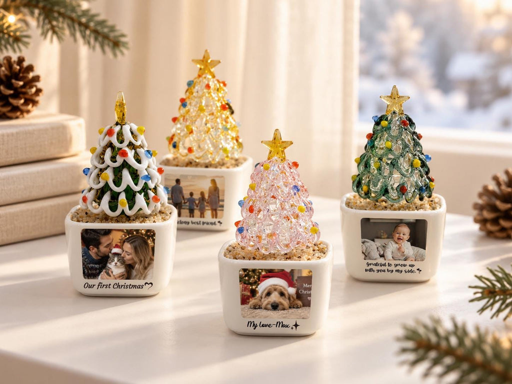 May include: Four decorative tabletop Christmas trees in white square ceramic planters. Each tree features a glass structure with colorful lights and a gold star topper. The planters display personalized photographs and text including Our first Christmas.