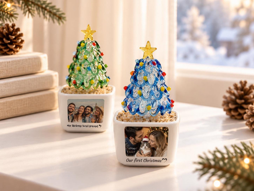 May include: Two glass Christmas tree ornaments in white square planters. One tree is green with multicolored lights and a yellow star, featuring a photo and the text My lifelong best friend. The other is blue with lights and a yellow star, featuring a photo and the text Our first Christmas.