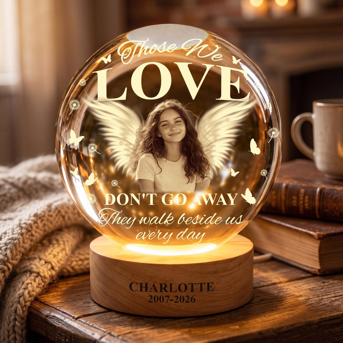 May include: A spherical glass memorial light featuring a portrait of a young person with angel wings, surrounded by butterflies and dandelions. The text reads "Those We LOVE DON'T GO AWAY They walk beside us every day" with "CHARLOTTE 2007-2026" on the base.