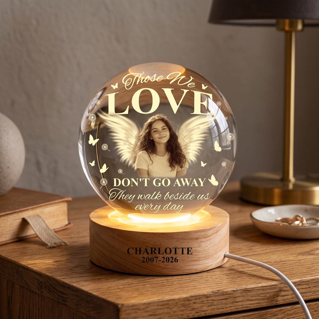 May include: A spherical glass night light on a round wooden base. The glass features a printed image of a person with angel wings, butterflies, and the text: Those We LOVE DON'T GO AWAY They walk beside us every day. The base reads: CHARLOTTE 2007-2026.
