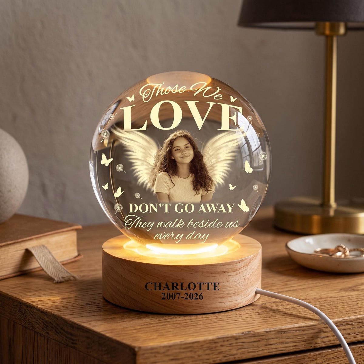 May include: A spherical glass night light on a round wooden base. The glass features a printed image of a person with angel wings, butterflies, and the text: Those We LOVE DON'T GO AWAY They walk beside us every day. The base reads: CHARLOTTE 2007-2026.