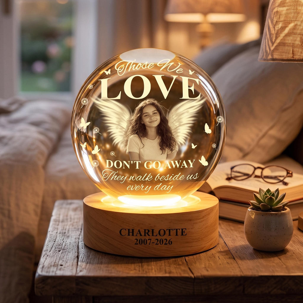 May include: A spherical glass memorial lamp featuring a photo of a person with angel wings, butterflies, and the text "Those We LOVE DON'T GO AWAY They walk beside us every day". The wooden base is engraved with "CHARLOTTE 2007-2026".