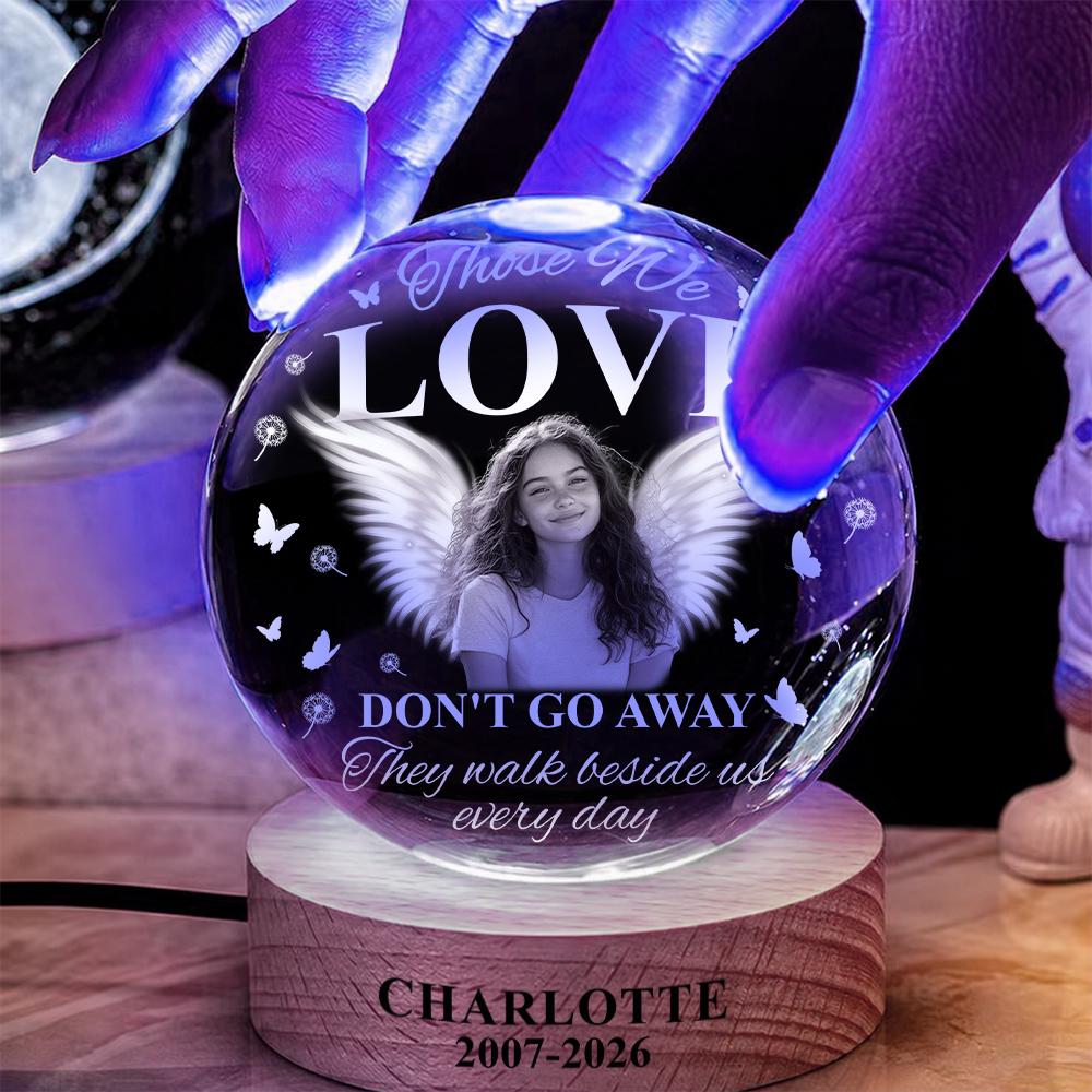 May include: A spherical glass ornament on a wooden base featuring a portrait of a person with angel wings. The text reads: Those We LOVE DON'T GO AWAY They walk beside us every day. The base is engraved with CHARLOTTE 2007-2026 and butterfly icons.