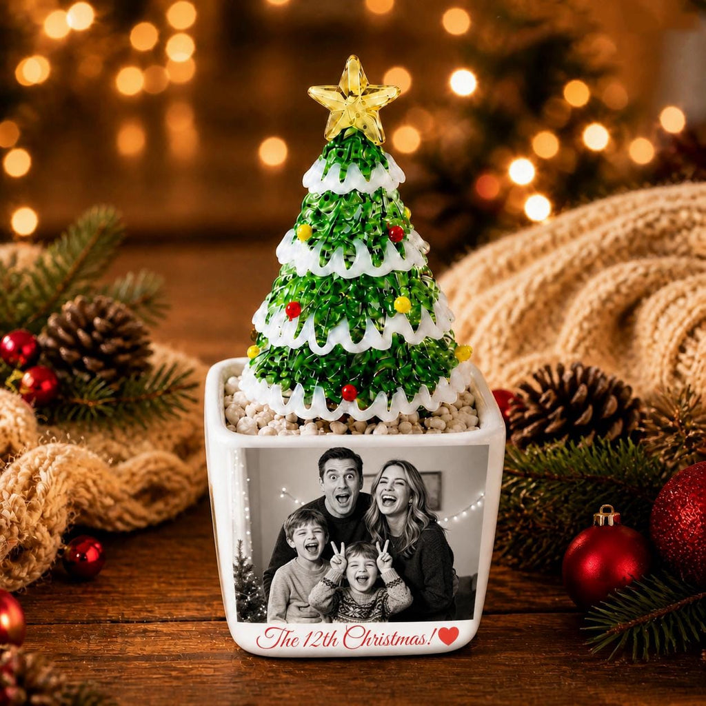 May include: A square white ceramic planter featuring a black and white family photograph and the text "The 12th Christmas!" with a red heart. A green glass Christmas tree with white snow-like accents and a yellow star sits on top of the planter.
