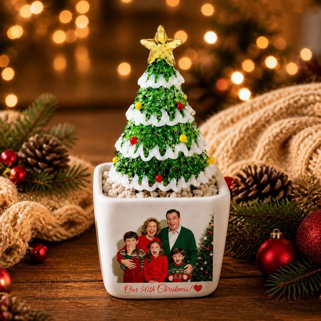 May include: A glass Christmas tree ornament with green branches, white snow-like accents, and small colorful spheres, topped with a yellow star. The tree sits in a white square planter featuring a printed family photo and the text Our 50th Christmas.