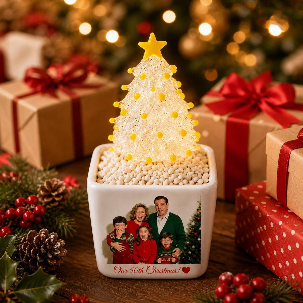 May include: A white square ceramic planter featuring a printed family photograph and the text Our 50th Christmas with a red heart. The planter holds a clear, textured glass Christmas tree ornament topped with a yellow star and yellow beads.