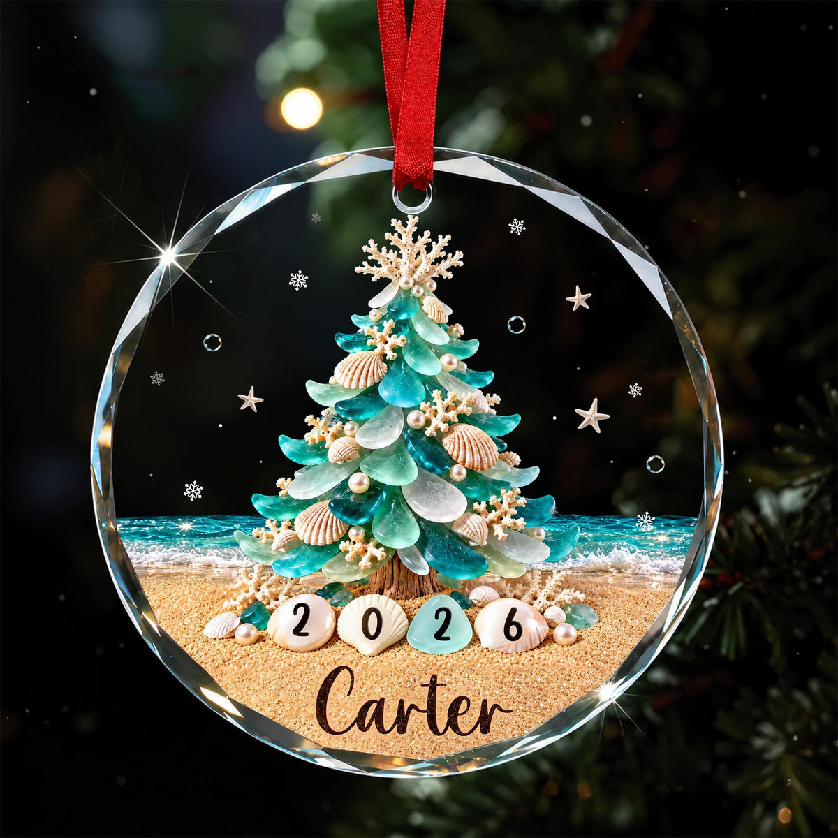 May include: A round, clear glass ornament featuring a printed design of a Christmas tree made from teal and white sea glass, seashells, and coral on a sandy beach. The year 2026 is printed on shells, and the name Carter is printed below.