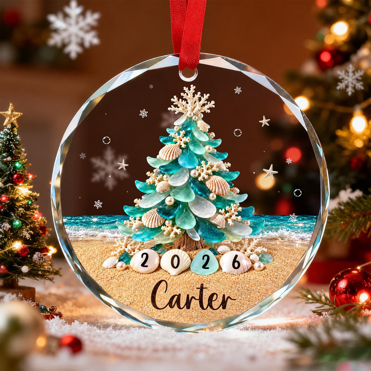 May include: A circular glass Christmas ornament featuring a coastal-themed tree made of sea glass, seashells, and coral on a sandy beach. The year 2026 is printed on shells at the base, with the name Carter written below in black script.
