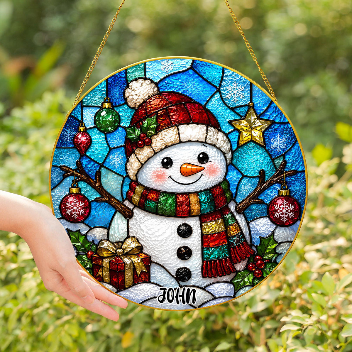 May include: A circular stained glass suncatcher featuring a snowman wearing a red hat and a multicolored scarf. The snowman is surrounded by blue glass, hanging ornaments, a gold star, and a gift box. The name JOHN is printed at the bottom.