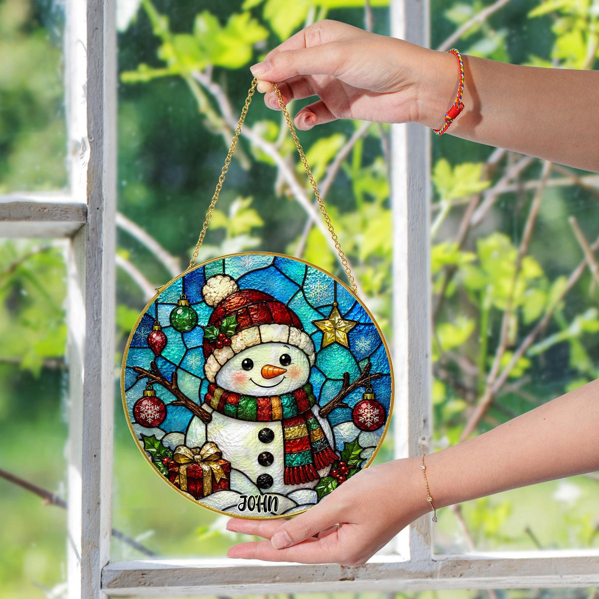 May include: A circular stained glass suncatcher featuring a snowman wearing a red hat and a multi-colored scarf. The background displays a blue geometric pattern with Christmas ornaments, a star, and holly. The name JOHN is printed at the bottom.