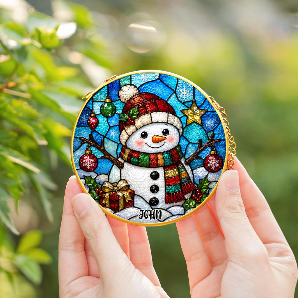 May include: A circular stained glass ornament featuring a snowman wearing a red hat and a multi-colored scarf. The background displays blue glass patterns with hanging ornaments, a gold star, and a gift box. The name JOHN is printed at the bottom.