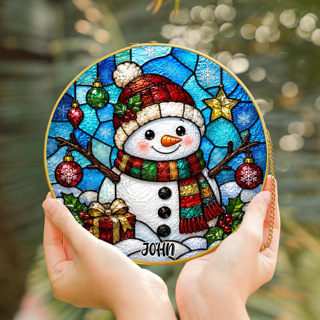 May include: A circular stained glass suncatcher featuring a snowman wearing a red hat and a multi-colored scarf. The design includes hanging ornaments, a gold star, a gift box, and holly leaves against a blue background with the name JOHN printed.