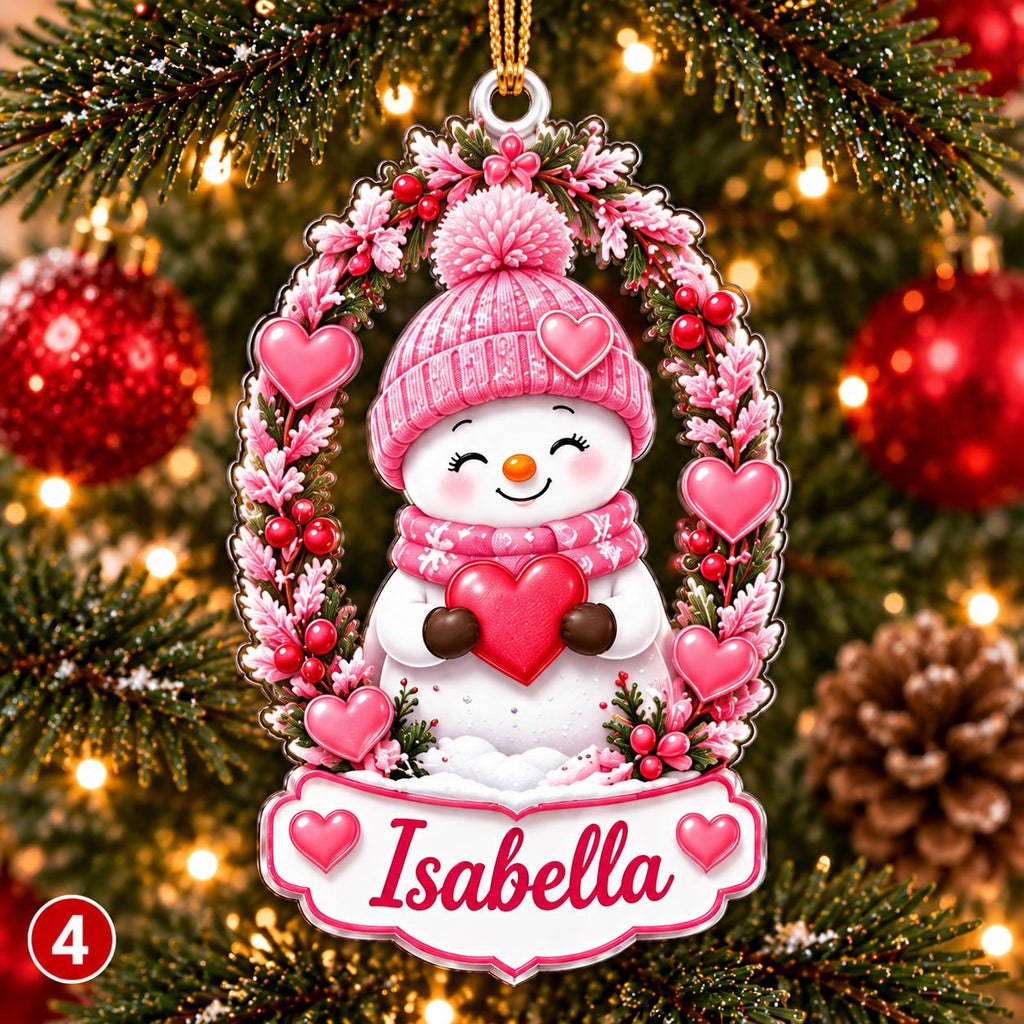 May include: A Christmas ornament featuring a white snowman wearing a pink knit hat and scarf, holding a red heart. The snowman is framed by a pink floral wreath with red berries and hearts. A white banner at the bottom displays the name Isabella.