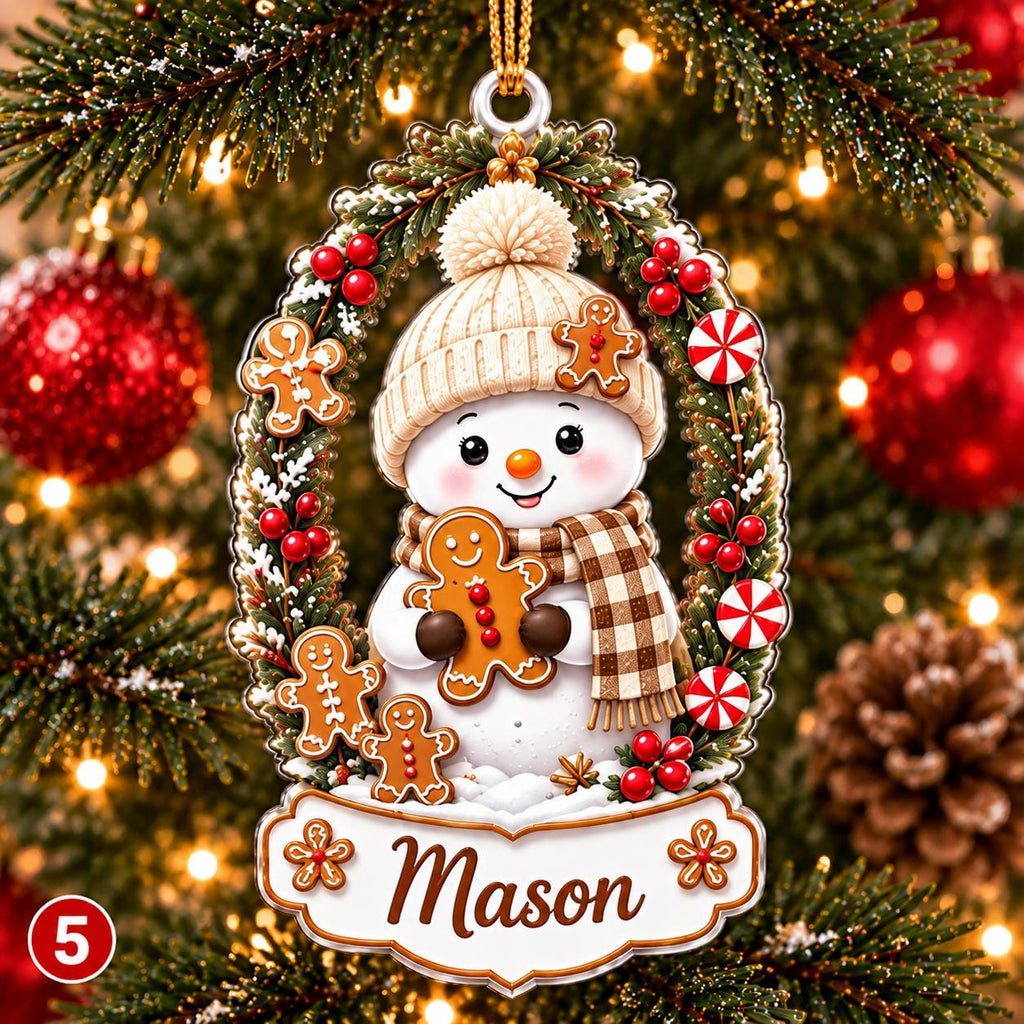 May include: An oval Christmas ornament featuring a snowman wearing a beige knit hat and a brown plaid scarf. The snowman holds a gingerbread cookie, surrounded by a wreath of pine branches, red berries, and peppermint candies. The name Mason is printed.