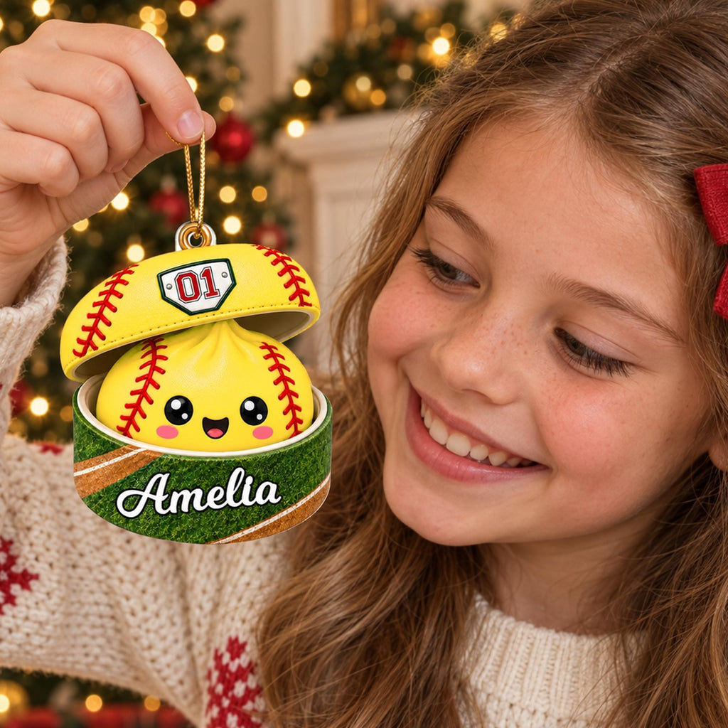 A young girl is holding a yellow ornament with a smiling face and the name "Amelia" written on it, smiling at the ornament.