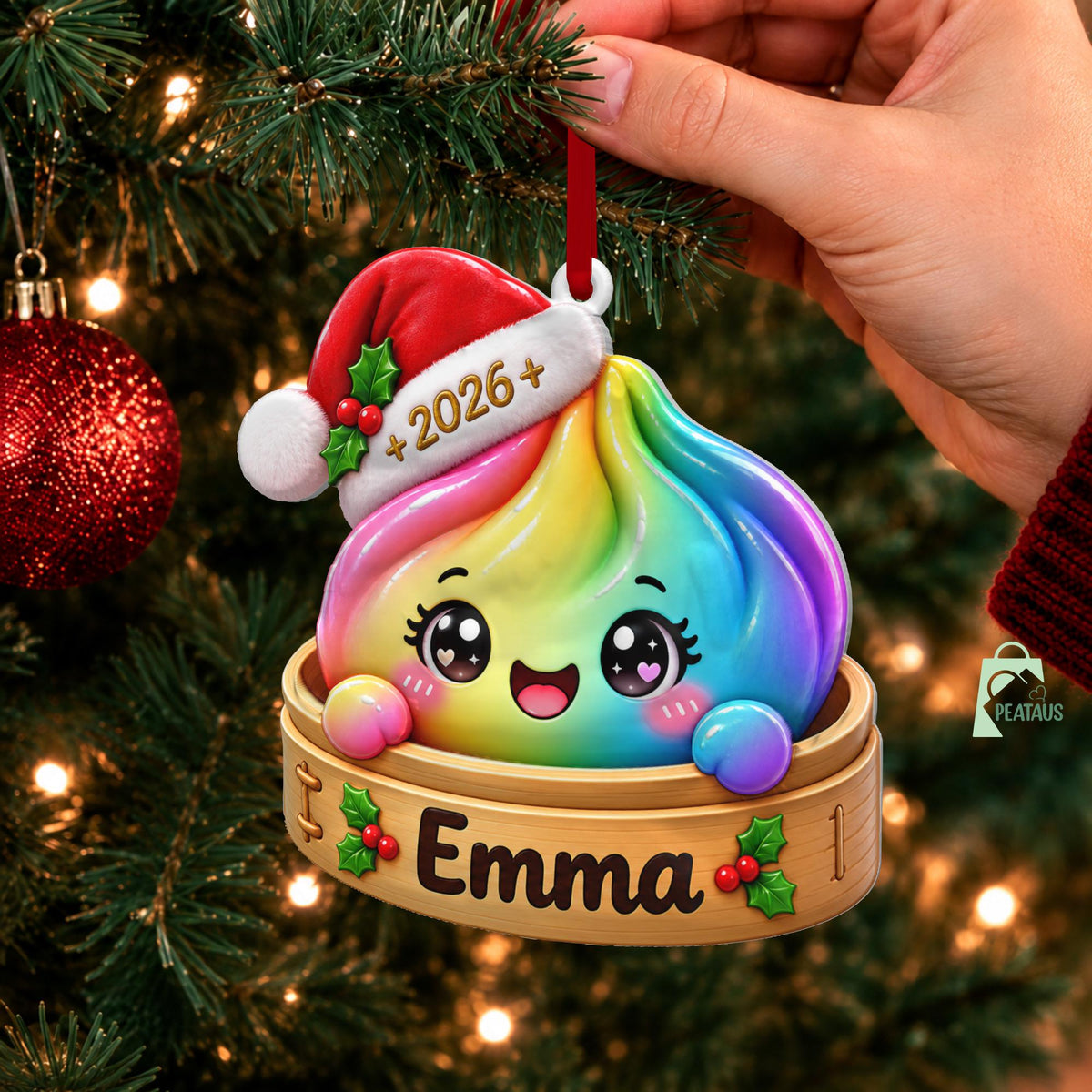 May include: A rainbow-colored dumpling ornament featuring a smiling face with large eyes, wearing a red and white Santa hat with the text 2026. The dumpling sits in a bamboo steamer basket labeled with the name Emma and decorated with holly berries.