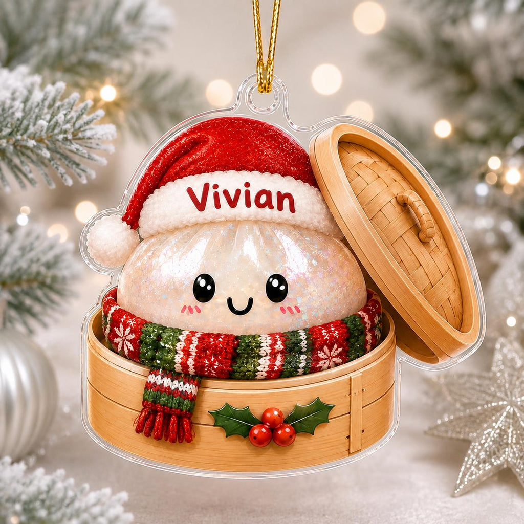May include: A clear acrylic Christmas ornament shaped like a bamboo steamer containing a smiling dumpling character. The dumpling wears a red Santa hat with the name Vivian printed on it and a red and green patterned scarf. A holly sprig is attached.