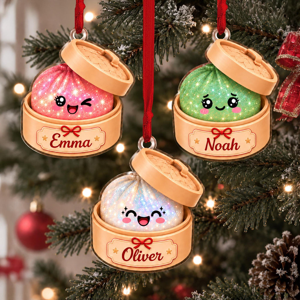 May include: Three hanging Christmas ornaments shaped like bamboo steamer baskets containing glittery, smiling dumplings. The pink dumpling is labeled Emma, the green one Noah, and the white one Oliver. Each ornament hangs from a red ribbon.