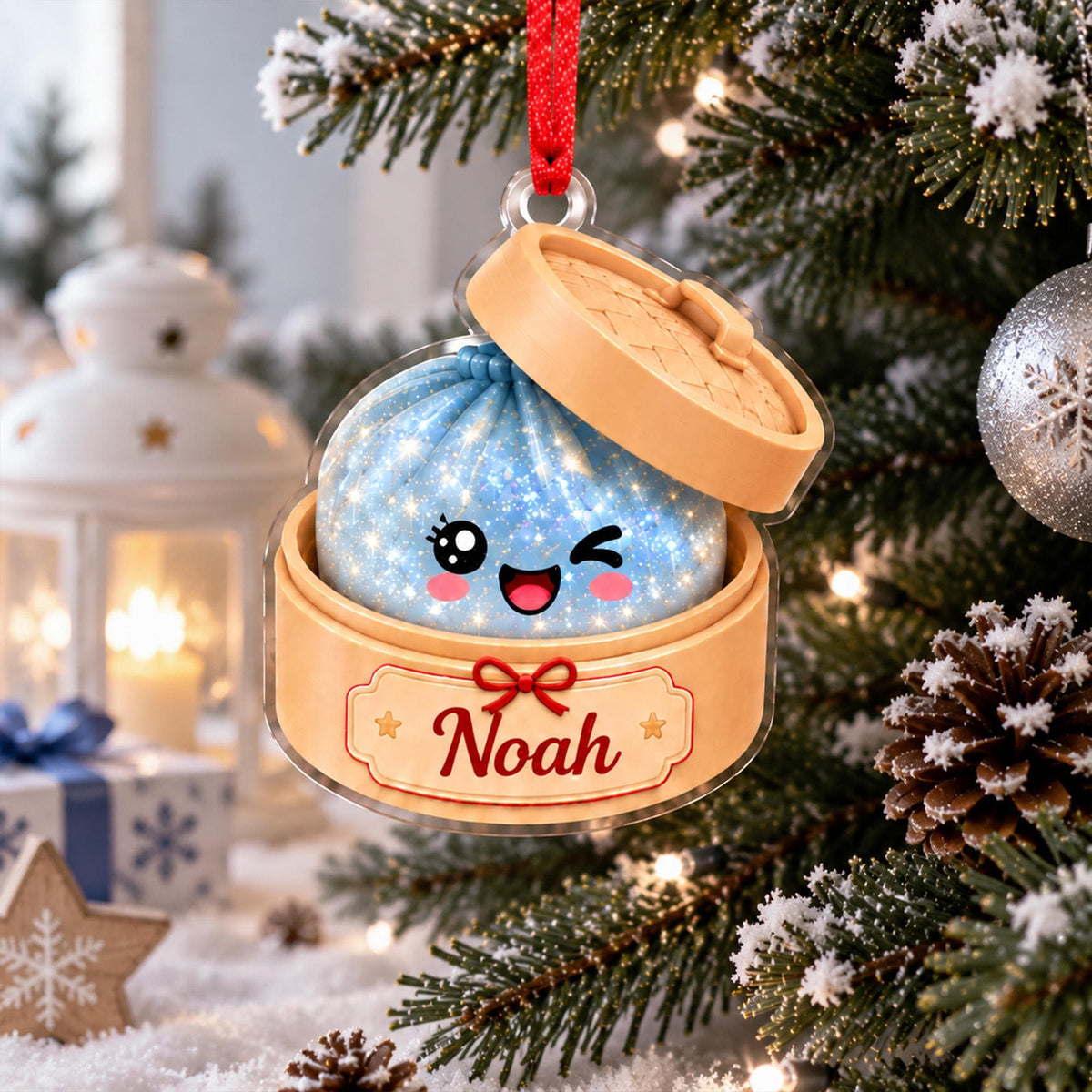 May include: A flat acrylic Christmas ornament shaped like a bamboo steamer basket containing a blue, glittery, winking dumpling character. The base of the steamer features a red ribbon graphic and the name Noah printed in a dark red script font.