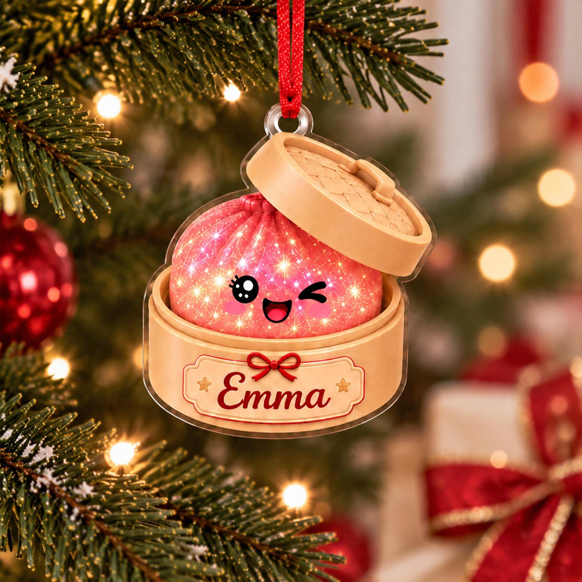 May include: A flat acrylic Christmas tree ornament shaped like a bamboo steamer basket containing a pink, sparkling dumpling with a winking face. The base of the steamer features a red bow and the name Emma printed in a cursive script font.