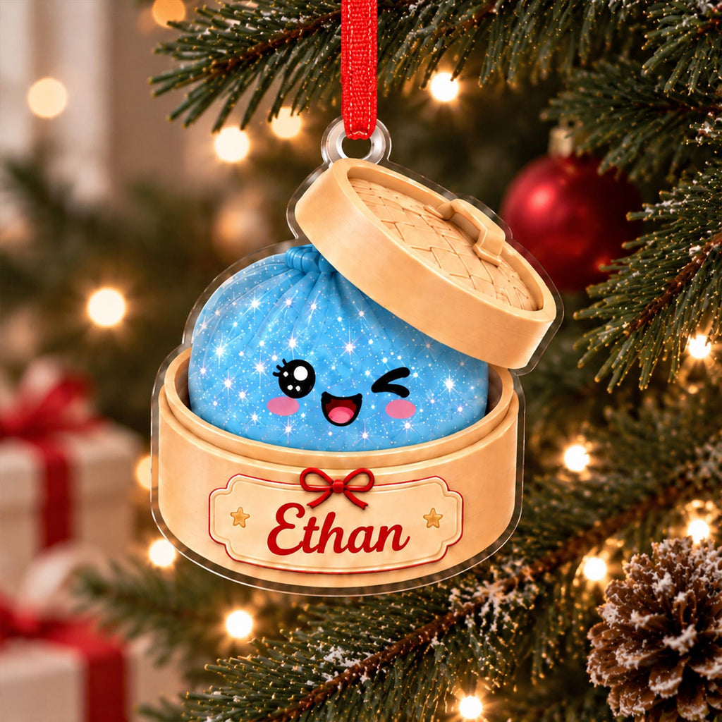 May include: A flat acrylic Christmas ornament shaped like a bamboo steamer basket containing a blue, sparkling, winking dumpling character. The base of the steamer features a cream-colored label with the name Ethan printed in red script.