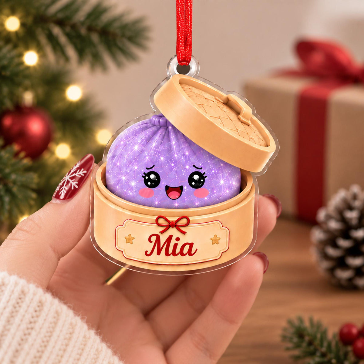 May include: A flat acrylic Christmas ornament shaped like a bamboo steamer basket containing a purple, glittery, smiling dumpling character. The base of the steamer features a label with the name Mia in red script and a small red bow graphic.