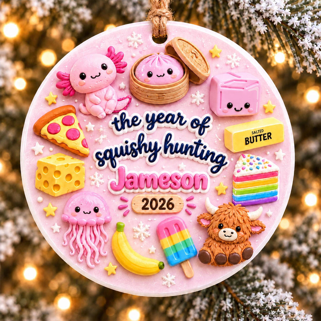 May include: A round pink ornament featuring the text the year of squishy hunting Jameson 2026. It is decorated with miniature figures including an axolotl, a dumpling, a slice of pizza, a block of cheese, a jellyfish, a banana, a popsicle, a highland cow, a rainbow cake, and a stick of salted butter.