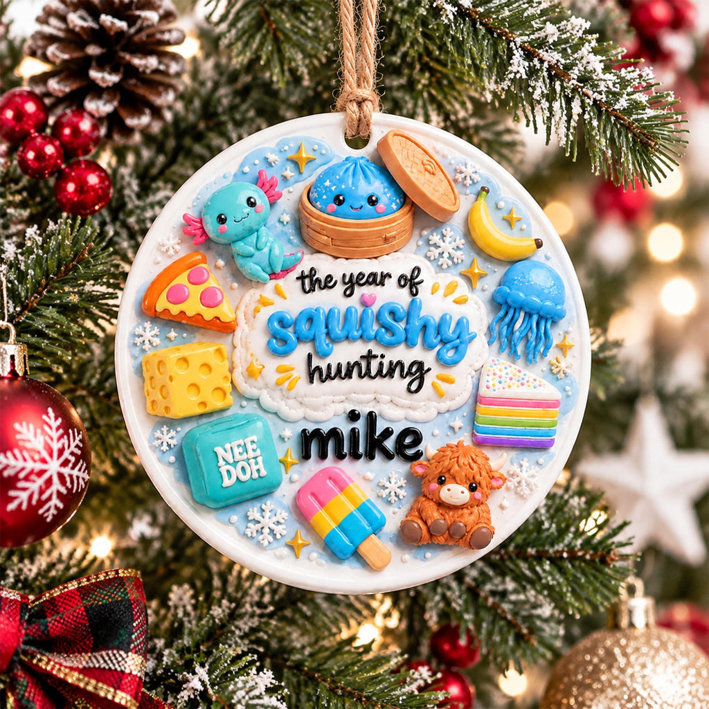 May include: A round white Christmas ornament featuring raised colorful figures including an axolotl, a dumpling, a slice of pizza, a banana, a jellyfish, a block of cheese, a rainbow cake, a popsicle, and a highland cow with the text the year of squishy hunting mike.