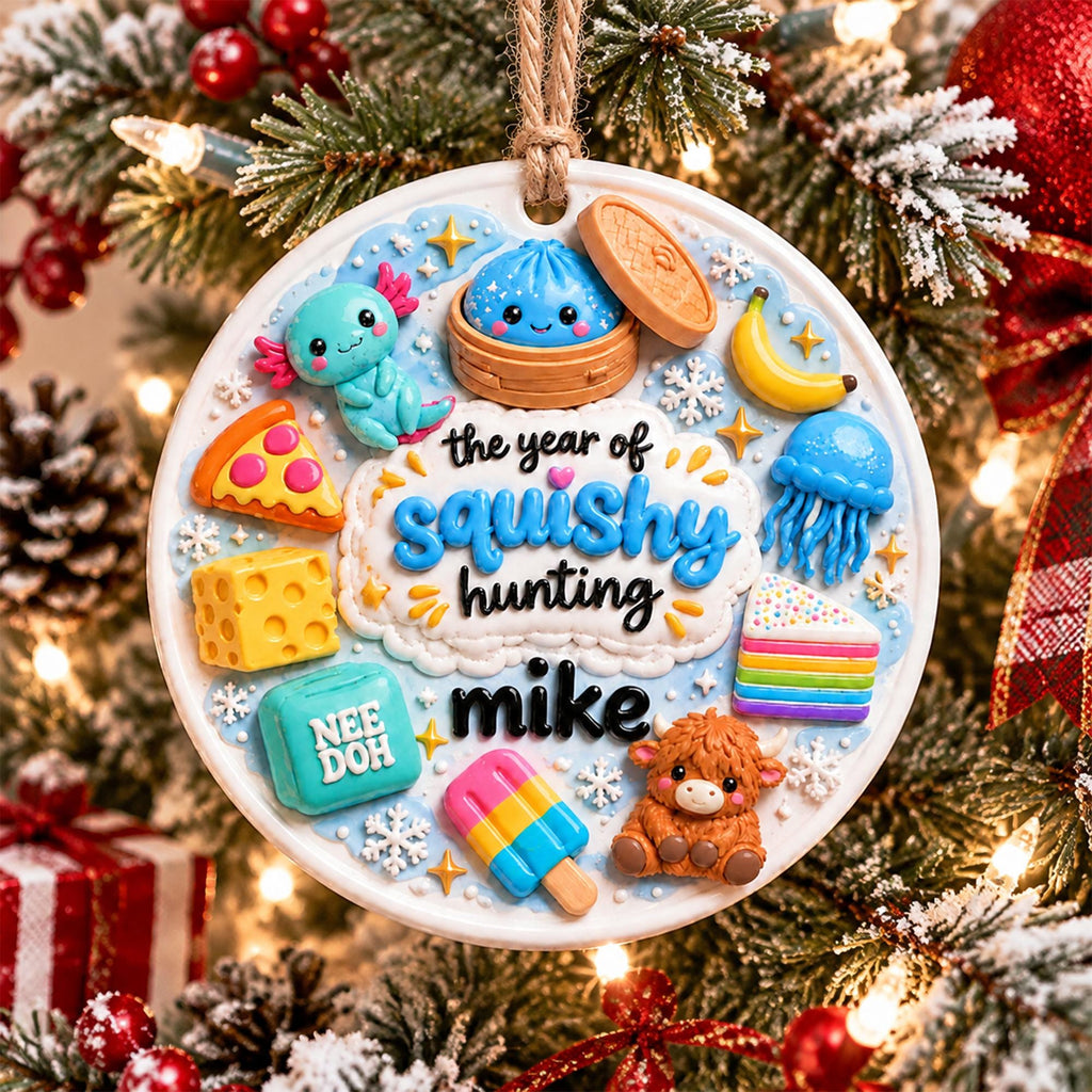 May include: A round white ceramic ornament featuring a light blue background with raised colorful figures including an axolotl, a dumpling, a banana, a slice of pizza, a block of cheese, a jellyfish, a rainbow cake, a popsicle, and a highland cow. The text reads the year of squishy hunting mike.