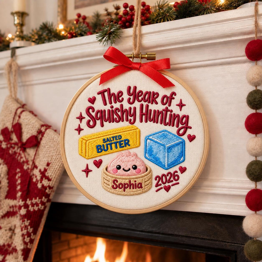 May include: A circular embroidery hoop featuring the text The Year of Squishy Hunting, a yellow stick of salted butter, a blue cube, and a pink dumpling in a bamboo steamer with the name Sophia and the year 2026, topped with a red ribbon.