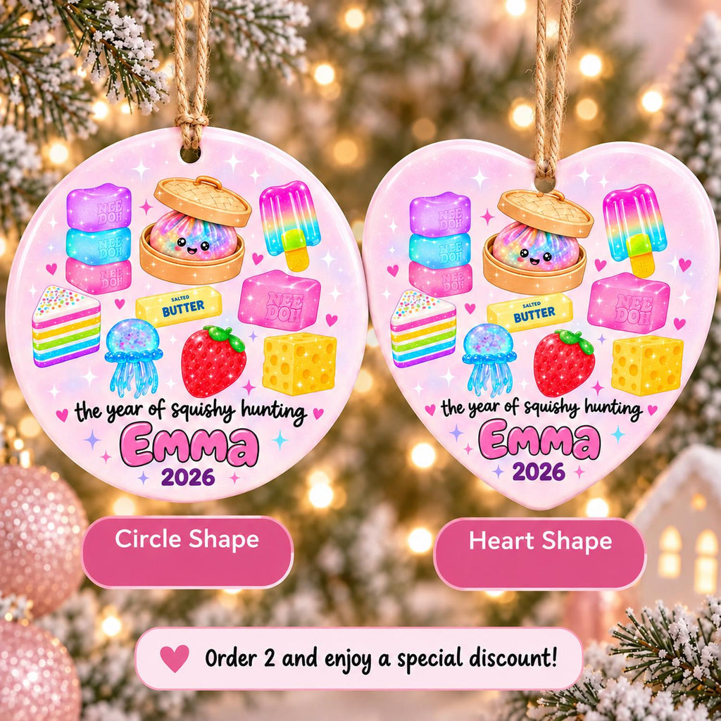 May include: Two ceramic ornaments, one circular and one heart-shaped, featuring a light pink background with colorful illustrations of squishy toys, a strawberry, and cheese. The text reads 'the year of squishy hunting', 'Emma', and '2026'.