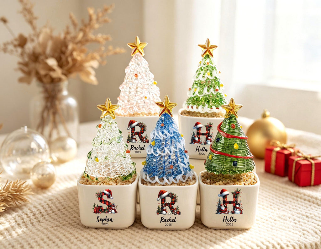 May include: Six miniature Christmas tree ornaments in square white ceramic pots. Each tree is topped with a gold star and features a unique color, including pink, green, and blue. The pots are personalized with letters, names, and the year 2025.