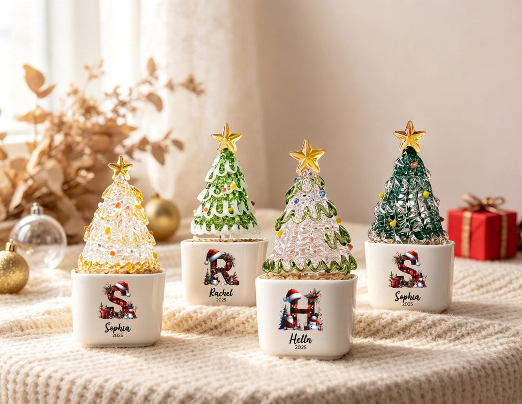 May include: Four miniature Christmas tree ornaments in white ceramic pots. Each tree has a gold star topper and colorful accents. The pots feature personalized letters, names like Sophia, Rachel, and Helln, and the year 2025 in black text.