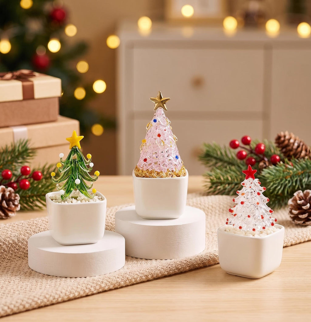 May include: Three miniature glass Christmas tree figurines in white square pots. One tree is green with yellow accents, one is pink with gold and blue accents, and one is clear with red accents. Each tree is topped with a small star ornament.