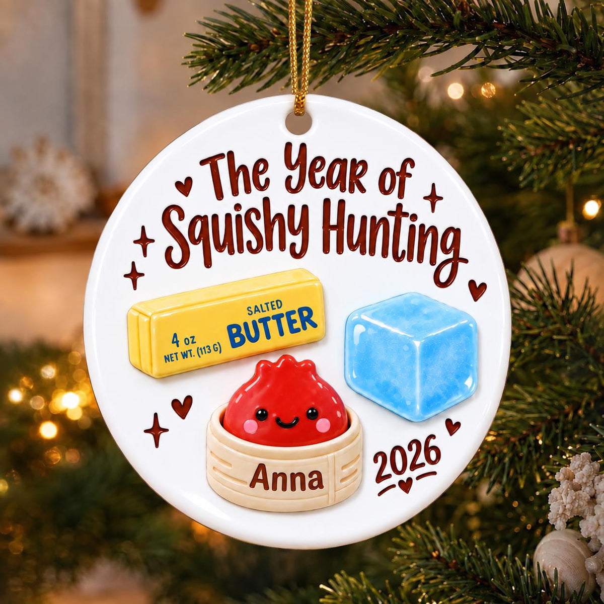 May include: A round white ceramic ornament with a gold string. The text reads The Year of Squishy Hunting, Anna, and 2026. It features illustrations of a yellow stick of salted butter labeled 4 oz, a blue ice cube, and a red dumpling in a steamer.