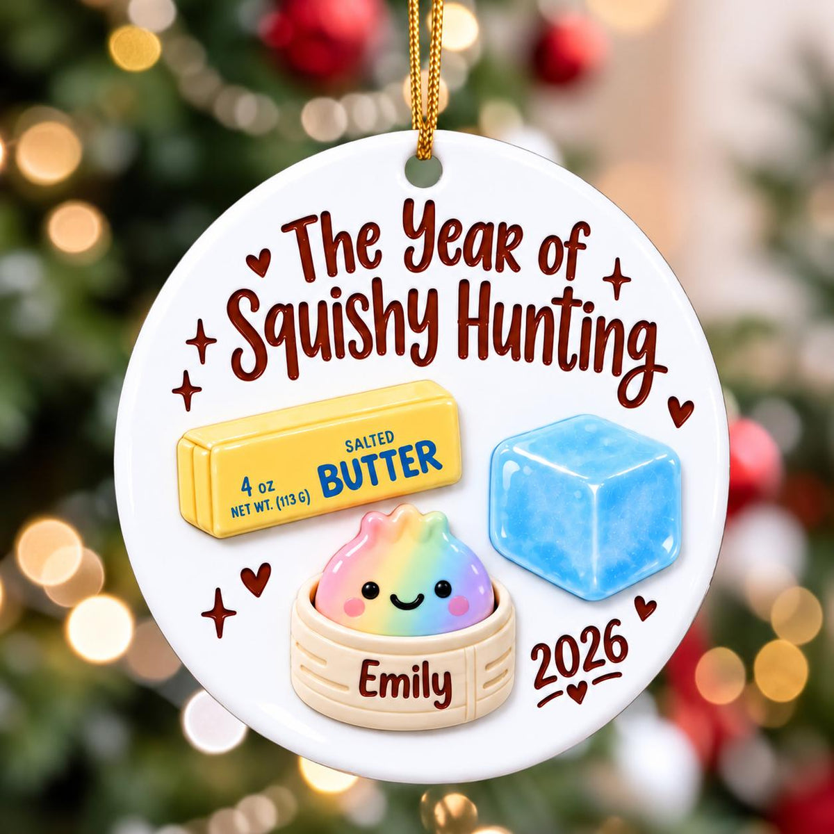 May include: A round white ceramic ornament featuring the text The Year of Squishy Hunting, a yellow stick of salted butter labeled 4 oz, a blue ice cube, and a rainbow-colored dumpling in a steamer basket labeled Emily with the year 2026.