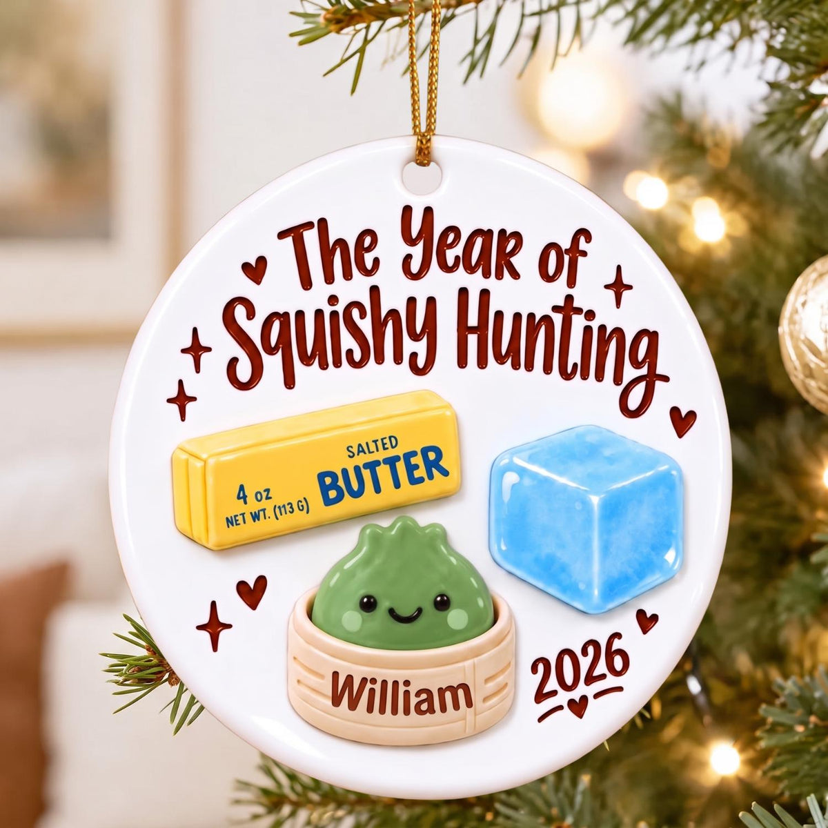 May include: A round white ceramic ornament featuring the text The Year of Squishy Hunting and 2026. It displays a yellow stick of 4 oz salted butter, a blue cube, and a green character in a beige steamer basket labeled William with red hearts.
