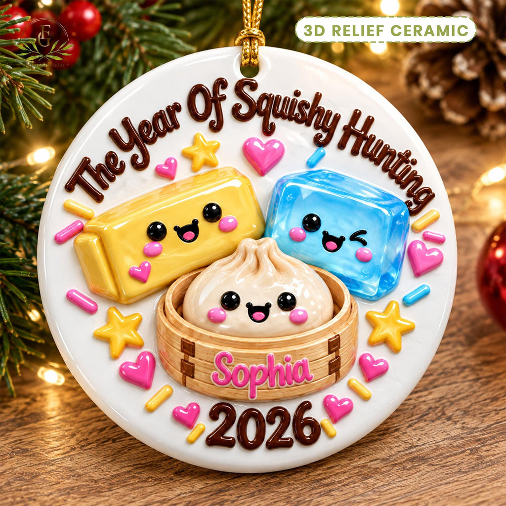May include: A round white 3D relief ceramic ornament featuring the text The Year Of Squishy Hunting, Sophia, and 2026. The design includes a yellow rectangular squishy, a blue squishy, and a dumpling in a bamboo steamer, all with faces.