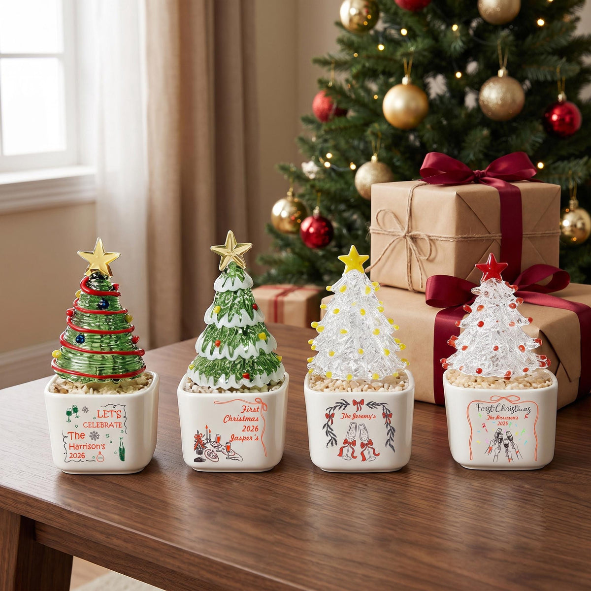 May include: Four small ceramic planters, each holding a decorative glass Christmas tree with a star topper. The white square pots feature festive illustrations and text including "Let's Celebrate," "First Christmas 2026," and "The Jeremy's."