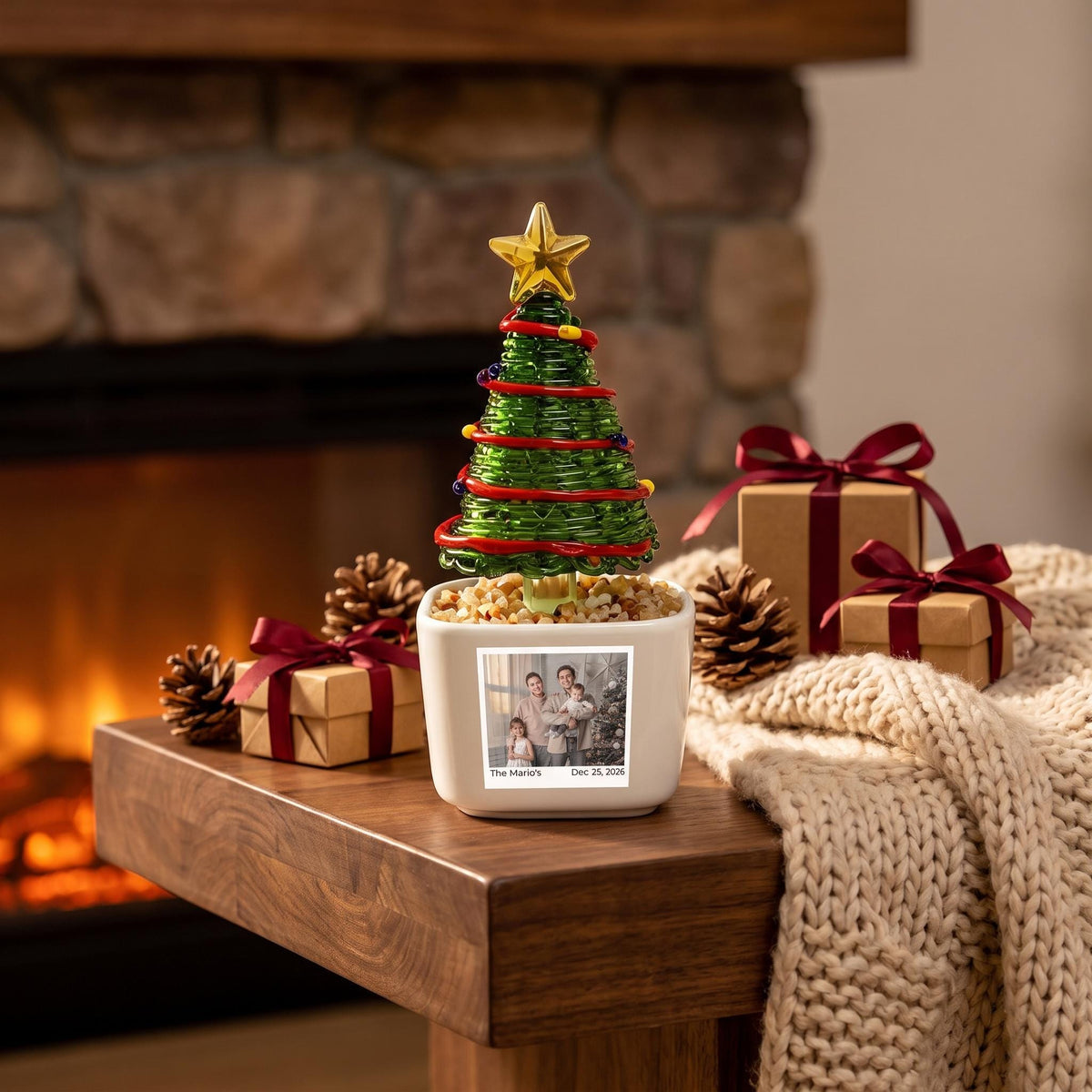 May include: A green wire Christmas tree ornament with a gold star topper, set in a white square planter filled with small stones. The planter features a black and white family photograph with the text The Mario's and Dec 25, 2026 printed below.