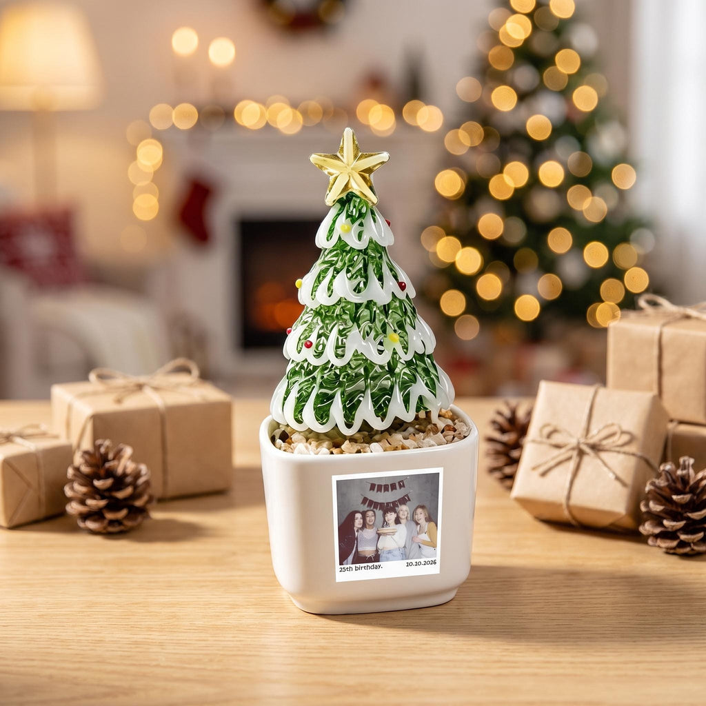 May include: A glass Christmas tree ornament with green and white swirls, topped with a gold star, sitting in a white square planter. The planter features a square photograph of five people with the text 25th birthday and 20.10.2026 printed below.