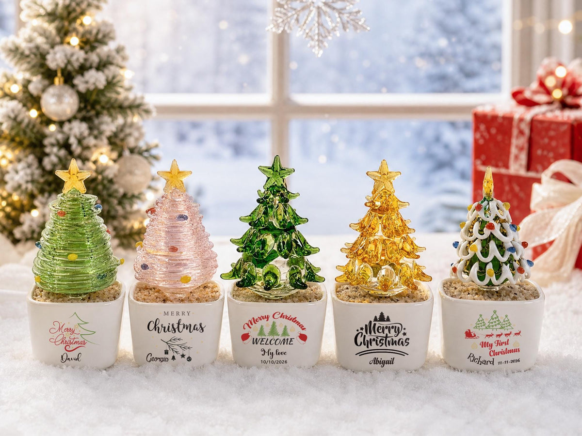May include: Five glass Christmas tree figurines in white ceramic pots. Each tree features a different color: light green, pink, dark green, yellow, and a multi-colored green tree with white accents. The pots are printed with holiday text and names.