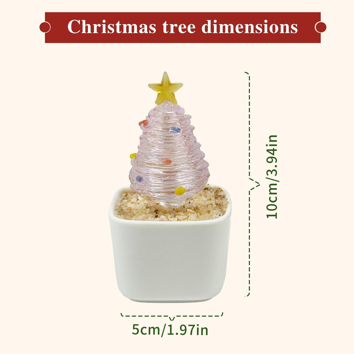 May include: A pink glass Christmas tree figurine with small colorful accents and a yellow star topper, set in a white square pot filled with sand. The tree measures 3.94 inches in height and the pot base measures 1.97 inches in width.