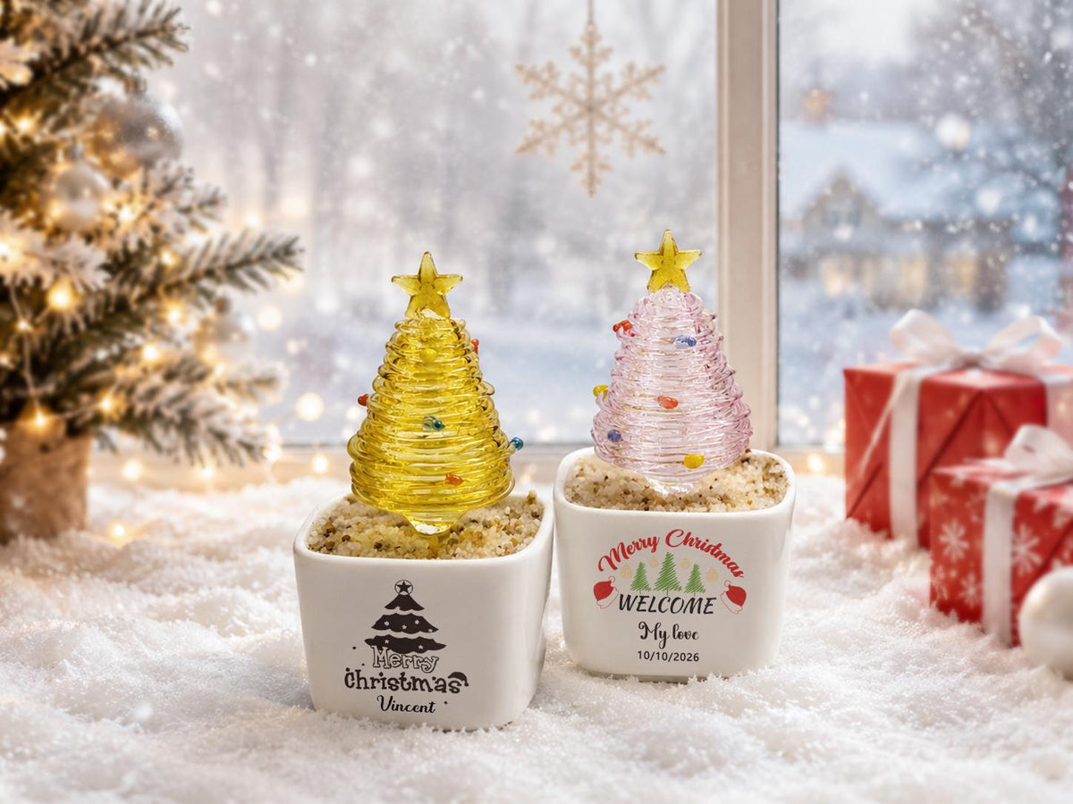May include: Two square white ceramic planters filled with sand, each topped with a spiral glass Christmas tree. The left planter features a black tree graphic and the text "Merry Christmas Vincent". The right planter has a colorful tree graphic and "Merry Christmas WELCOME My love 10/10/2026".
