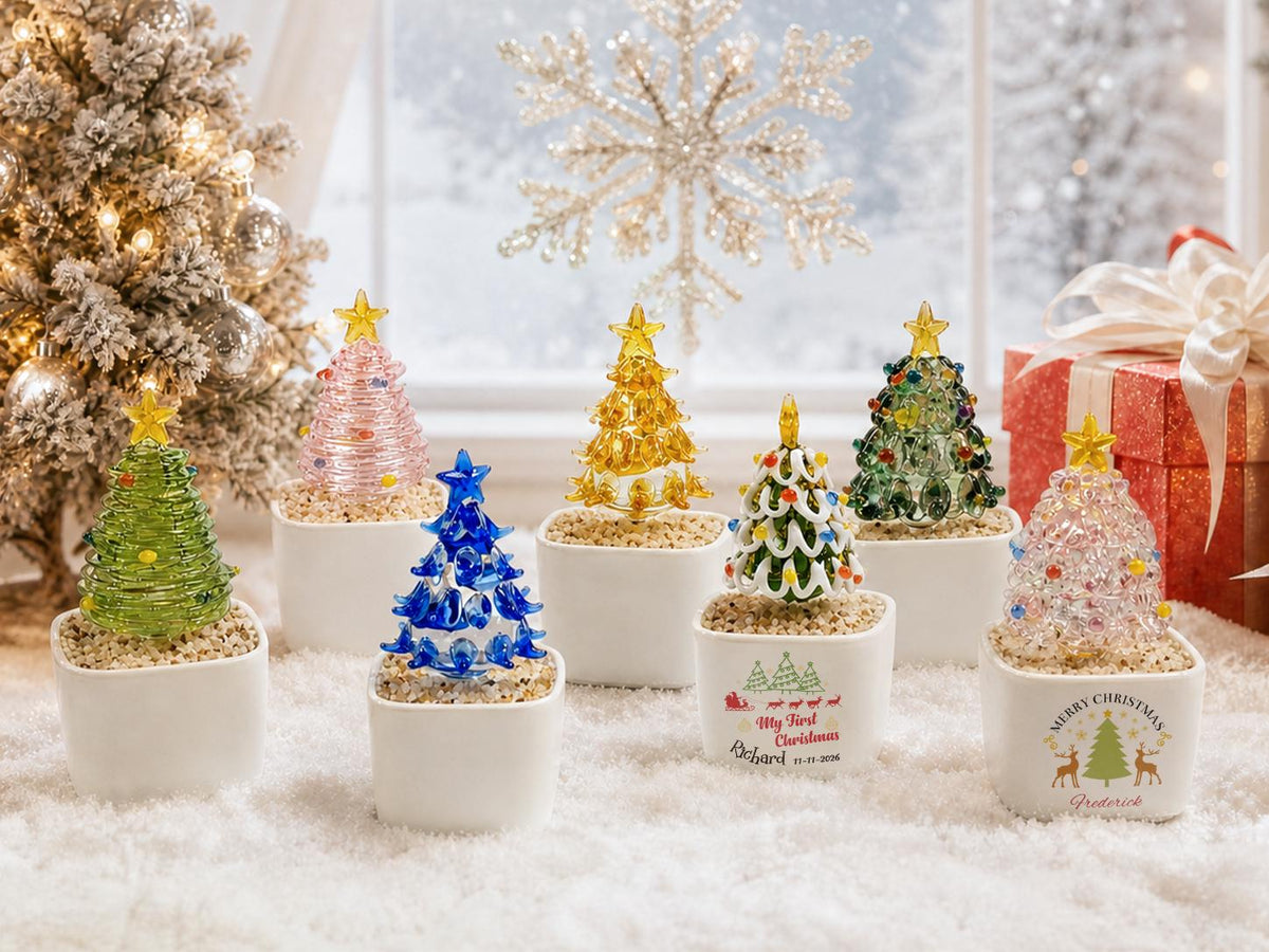 May include: A collection of six miniature glass Christmas trees in various colors, each topped with a yellow star and set in a small white square ceramic planter filled with pebbles. Two planters feature printed holiday text and graphics.