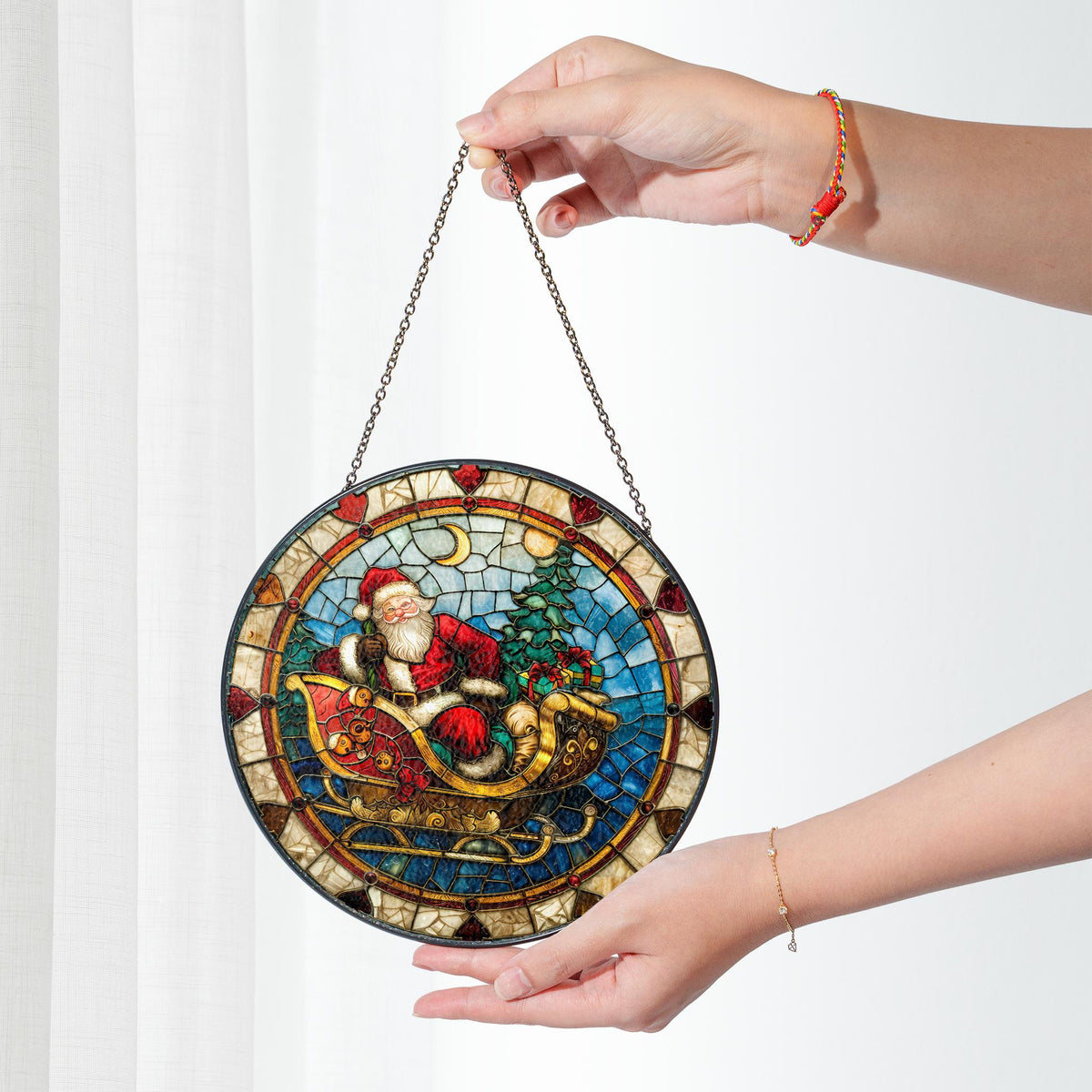 May include: Round stained glass window hanging featuring a colorful depiction of Santa Claus riding in a sleigh pulled by reindeer. The stained glass is framed in a dark metal frame and has a chain for hanging.