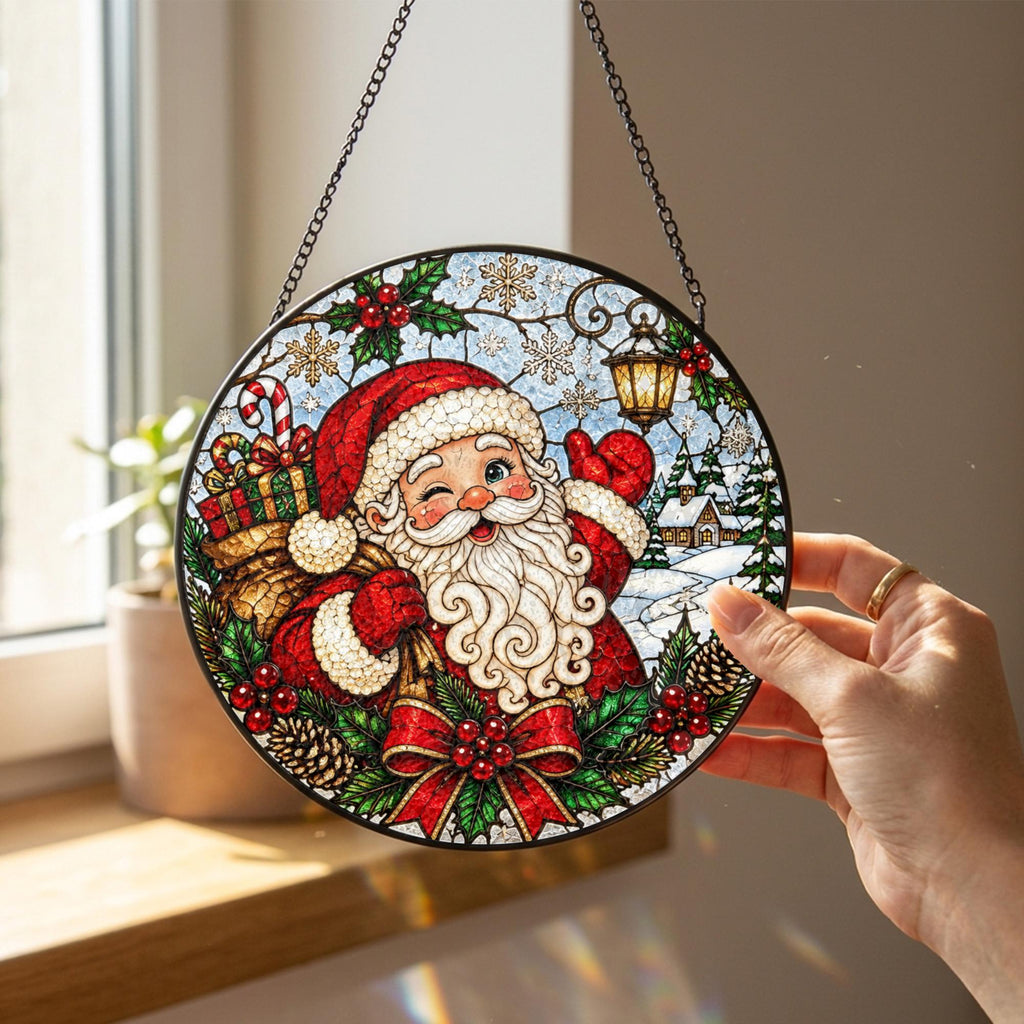 May include: A circular stained glass suncatcher featuring a winking Santa Claus with a white beard, red hat, and coat. He carries a gift-filled sack. The design includes holly, pinecones, a lantern, and snowflakes, all framed in black metal with a chain.