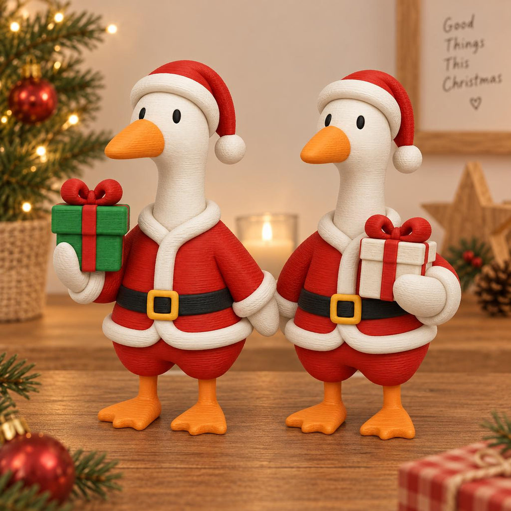 May include: Two white goose figurines wearing red and white Santa Claus outfits with black belts and yellow buckles. Each goose wears a matching Santa hat and holds a small gift box, one green with a red bow and one white with a red bow.