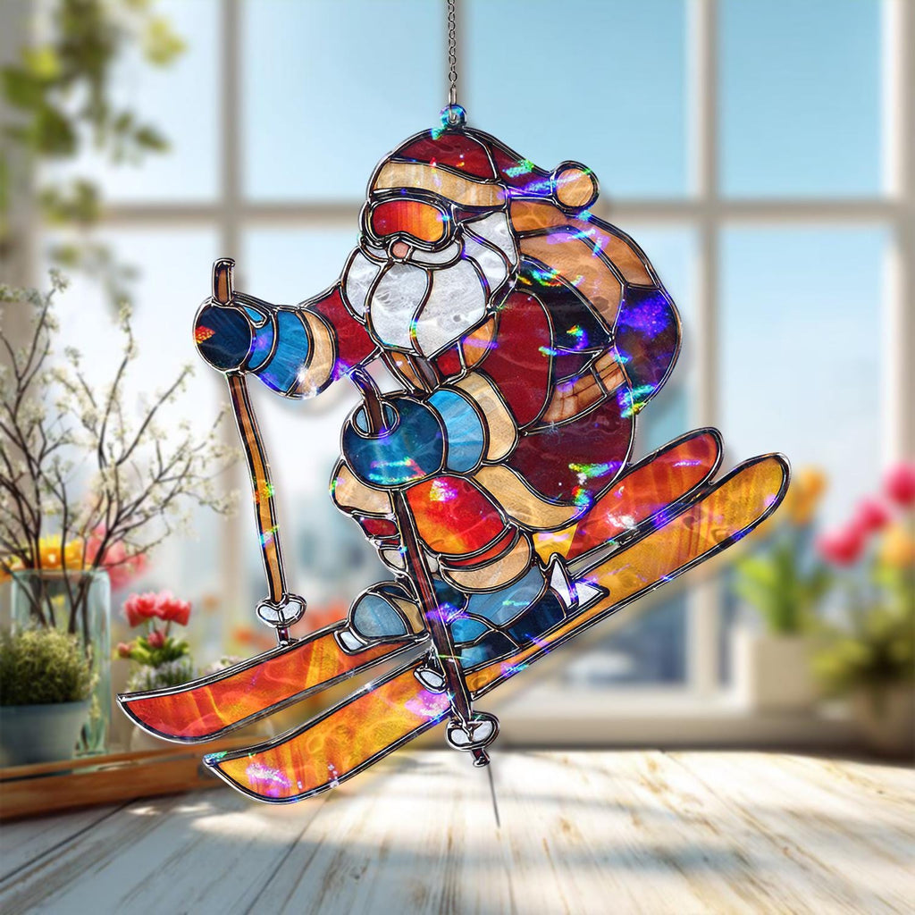 May include: A stained glass Christmas ornament depicting Santa Claus skiing. The ornament features a colorful design with red, blue, orange, and white hues. Santa is wearing a red hat and suit, with skis and poles. The ornament is hanging from a silver chain.