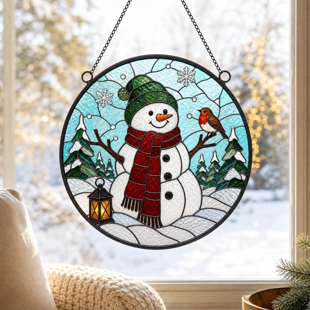 May include: A circular stained glass suncatcher featuring a white snowman wearing a green hat and a red scarf, standing in a snowy landscape with green pine trees, a small yellow lantern, and a brown robin, all suspended by a black metal chain.